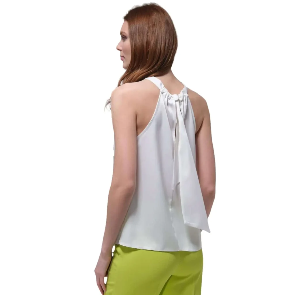Gretta sleeveless white party top with high neck and back tie detail, paired with lime green pants for a stylish, trendy look.