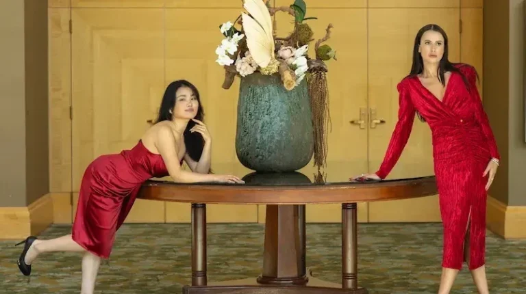 Stylish women in red dresses, posing gracefully at a luxury event, showcasing elegant evening wear and formal attire. One model wears a sleek satin dress, while the other stuns in a textured red dress with a sophisticated silhouette. Perfect for cocktail parties, upscale gatherings, or glamorous nights out. Motrati's fashion collection combines timeless elegance with modern chic for any special occasion.