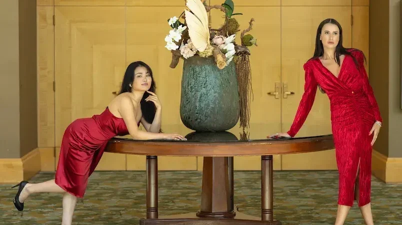 Stylish women in red dresses, posing gracefully at a luxury event, showcasing elegant evening wear and formal attire. One model wears a sleek satin dress, while the other stuns in a textured red dress with a sophisticated silhouette. Perfect for cocktail parties, upscale gatherings, or glamorous nights out. Motrati's fashion collection combines timeless elegance with modern chic for any special occasion.