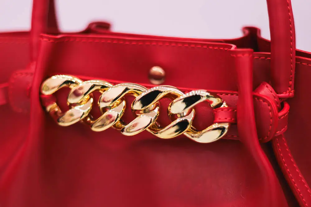 Close-up of a chic red leather handbag with a gold chain detail and vibrant navy and red scarf accessory, adding an elegant touch to the stylish design.