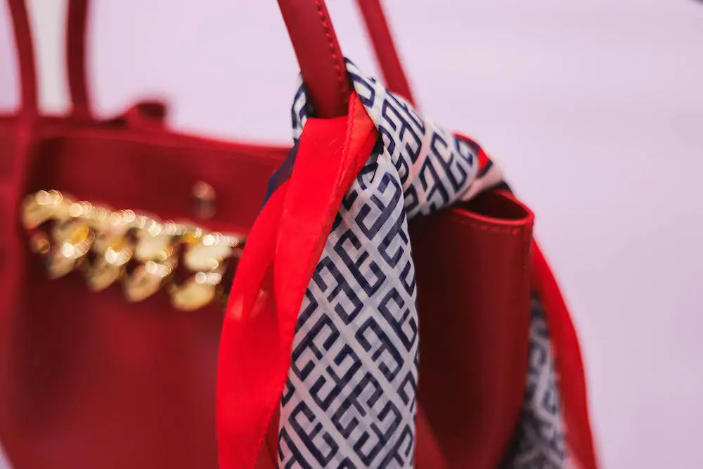 Red leather handbag with gold accents, styled with a chic navy and white patterned scarf for a sophisticated look