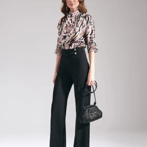 Model wearing Maje women's high-waisted wide-leg trousers in black, styled as tailored work pants with an animal print blouse and black handbag.