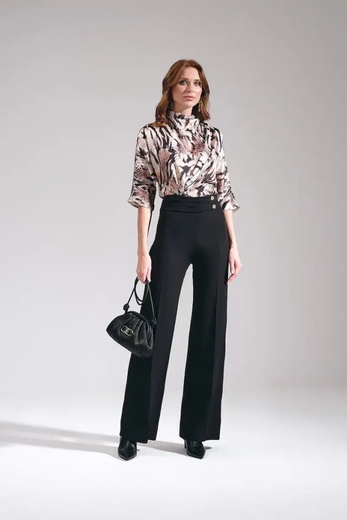 Model wearing Maje women's high-waisted wide-leg trousers in black, styled as tailored work pants with an animal print blouse and black handbag.